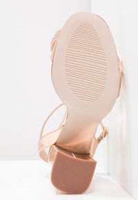 Sandale beige pour femme vue par la semelle, montrant un petit talon bloc et un motif de grip texturé en dessous.