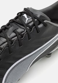 Scarpa da calcio nera con upper in pelle testurizzata, accentuata da strisce bianche e lacci neri. Include un piccolo logo bianco sul lato.
