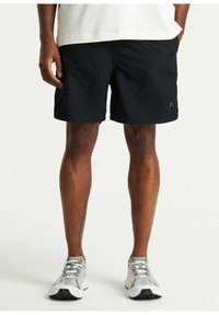 Shorts neri realizzati in tessuto leggero con frontale piatto, tasche laterali e un piccolo logo sull'orlo sinistro; abbinati a scarpe da corsa grigie.