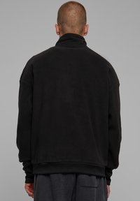 Svart fleece sweatshirt med høy krage, senkede skuldre og ribbede mansjetter. Jevn tekstur, avslappet passform, minimalistisk design.