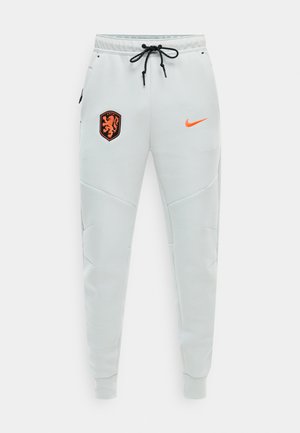 Hvide atletikbukser med sort snøre, hollandsk løveemblem på venstre hofte og orange Nike-swoosh på højre hofte, tilspidsede manchetter ved anklerne.