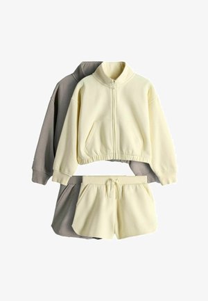 Dvi kostiumų rinkiniai iš fliso su raišteliais sunkintomis trumpomis kelnėmis ir striukėmis su užtrauktukais, vienas kremine spalva, kitas tamsiai pilka.