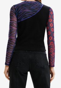 Langärmliges Oberteil mit einem schwarzen gerippten Körper, oberen Bereich mit lila und schwarzem Tigerprint sowie transparenten Ärmeln mit roten Blumen- und Leopardenmustern.