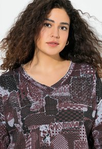 Langarm V-hals top in bordeauxrood en grijs, met een genaaide patchworkontwerp met verschillende patronen en details, gemaakt van zachte stof.