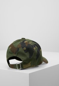 Camo baseball cap in green and brown tones, made of cotton. Features a curved brim and an adjustable strap at the back.