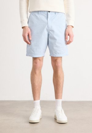 Light blue cotton shorts with a straight cut, featuring front pockets and a button closure, paired with white sneakers and crew-length socks.