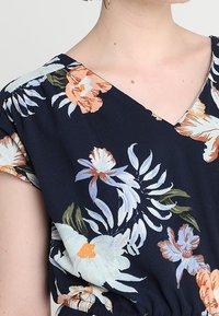 Námořnická blůza s květinovým vzorem, v výstřihem do V a krátkými rukávy; zdobena světle zbarvenými květinami a zelenými listy; texturovaná látka.