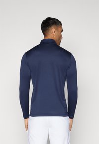 Hosszú ujjú sötétkék pólóing, texturált anyagból, gallérral és slim fit kialakítással, világos színű nadrággal párosítva.