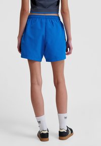 Blå idrottsshorts med elastisk midja, knälång klippning och slät textur. Kombinerade med vita strumpor och svarta sneakers med beige sulor.