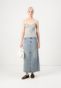 Débardeur gris à côtes avec bord blanc et cordon de serrage, associé à une jupe maxi en denim bleu clair, complété par des chaussures à imprimé léopard et un sac à main blanc.