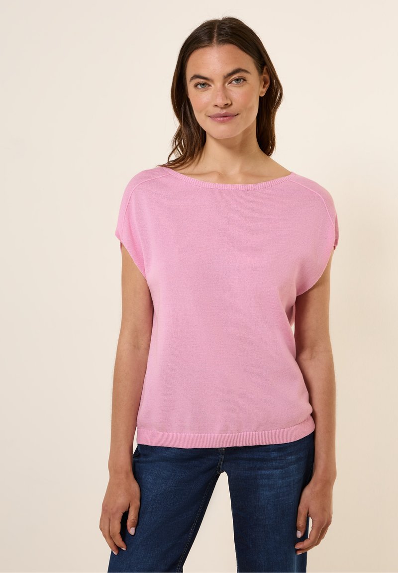 Ljusrosa kortärmad tröja med lös passform, rund halsringning och ribbad fåll. Buren med mörkblå jeans. Mjuk textur.