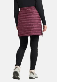 Maroon geïsoleerde rok met een gevoerd patroon, elastische taille, zijslitsen, gecombineerd met zwarte leggings en enkellaarsjes. Glad, glanzend materiaal.