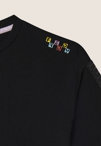 Camiseta de algodón negra con letras de bloque coloridas "FREDY" en el hombro, con sutiles rayas texturizadas en la manga.