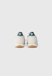 White and beige athletic shoes with suede and mesh materials. Green accent on the heel with an embossed logo. Gum rubber outsole.