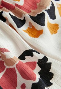 Tissu à motif floral comprenant des couleurs rose, orange, noir et crème. Tissage texturé avec des nervures visibles et une qualité de drapé souple.