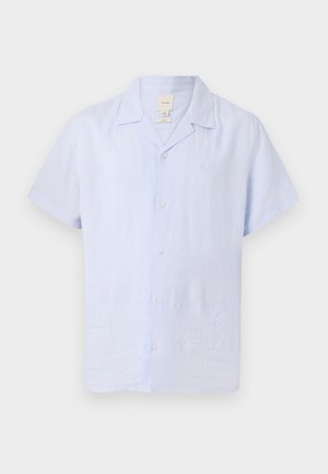 Chemise bleu clair à manches courtes avec col campagnard et logo discret sur la poitrine, sur fond uni.