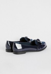 Mocassini in vernice blu navy con dettagli in ecopelle scamosciata, suola piatta e fiocco sulla parte frontale. Texture liscia e design arrotondato.
