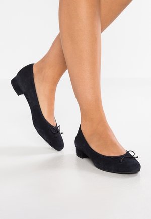Ballerines en suede noir avec un petit talon, présentant un bout arrondi et un détail de nœud décoratif à l'avant. Texture lisse.