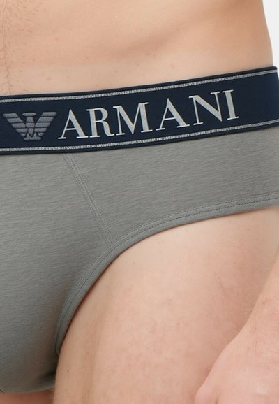 Slip grigio in cotone con vita blu navy e scritta "ARMANI" in lettere argentate e logo. Tessuto liscio, design aderente e taglio classico.