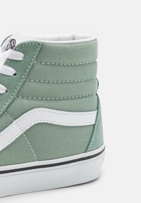 Wysokie sneakersy z jasnozielonej tkaniny z białymi akcentami, z wyściełanym kołnierzem, białymi sznurówkami i tagiem z logo w czarno-białym kolorze.
