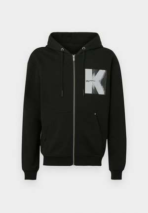 Svart hettejakke med glidelås, frontlomme, snor i hetten og et grafisk firkantmotiv med en stilisert 'K' og vertikale hvite linjer.