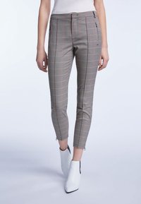 Pantalon court à carreaux beige, noir et rouge, coupe slim, poches avant, zips aux chevilles, assorti à des bottines blanches.