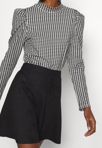 Schwarz-weiße karierte Bluse mit hohem Kragen und Puffärmeln, kombiniert mit einem kurzen schwarzen Rock. Strukturierter Stoff, taillierte Passform.