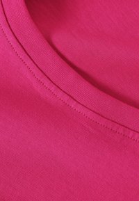Fuchsia bomuldsstof med en glat tekstur, der har en rund halsudskæring og flade sømme, der fremhæver dens bløde overflade og livlige farve.