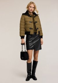 Olivově zelená zateplená bunda s černými akcenty, vysokým límcem a stahovacími uzávěry; černá kožená mini sukně; černé kozačky po kolena; malá černá kabelka.
