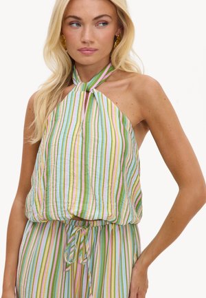 Femme blonde portant un top sans manches à col halter et un pantalon assorti avec des rayures verticales multicolores aux tons pastel.