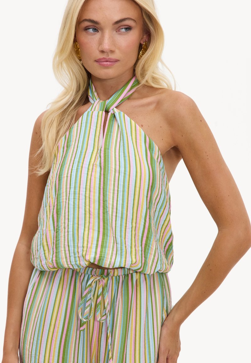 Femme blonde portant un top sans manches à col halter et un pantalon assorti avec des rayures verticales multicolores aux tons pastel.