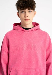 Różowa, oversize'owa bluza z kapturem, z wytłoczonym w tonacji napisem "ASCENSION", sznurkiem w kapturze oraz przednią kieszenią typu kangur z teksturowanym wykończeniem.