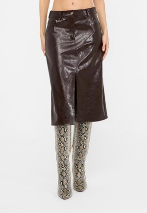 Glänzender dunkelbrauner Leder-Midirock mit Frontschlitz, kombiniert mit kniehohen beige-schwarzen Stiefeln mit Schlangenprint.