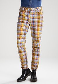 Flerfärgade rutiga byxor med mönster i gult, rött, blått och vitt; slim fit med fickor; bärs med svarta skor.