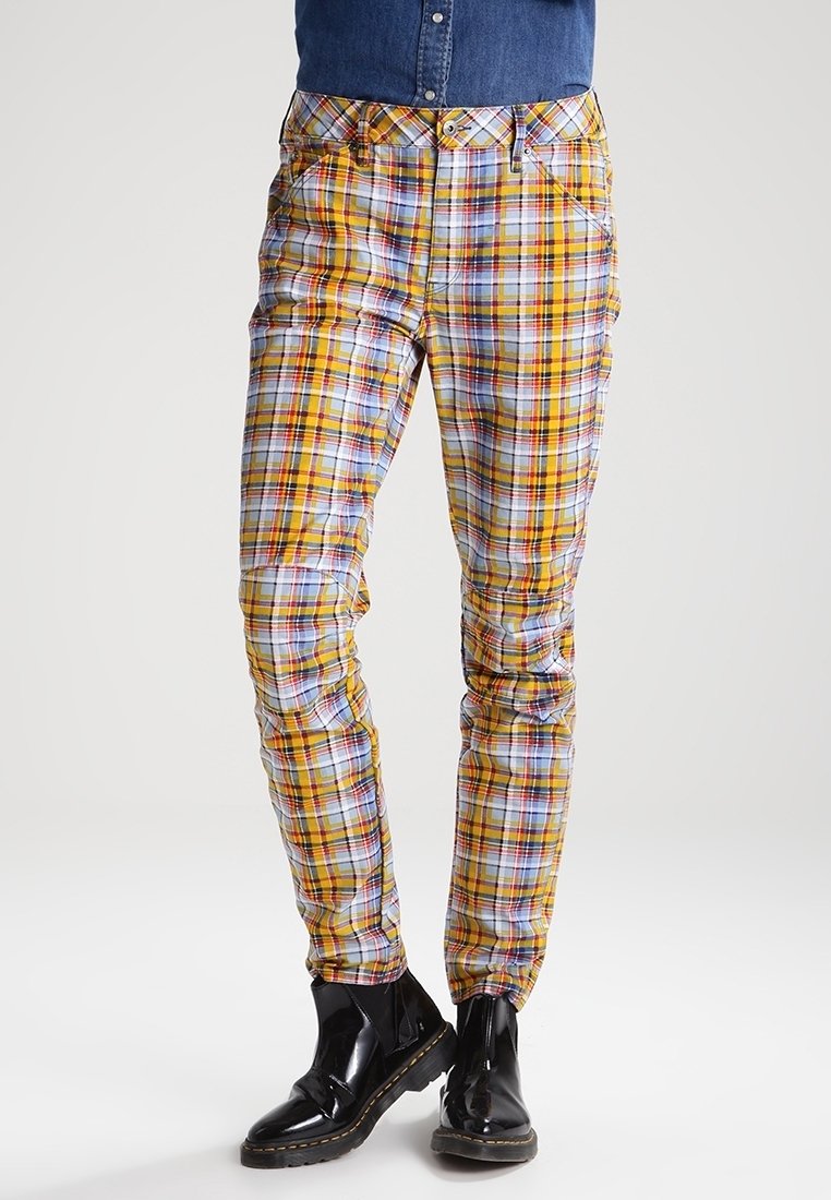 Flerfärgade rutiga byxor med mönster i gult, rött, blått och vitt; slim fit med fickor; bärs med svarta skor.