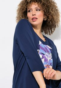 Marineblaues kurzärmliges Oberteil mit einem farbenfrohen abstrakten grafischen Design auf der Vorderseite. Glatter Stoff mit lockerer Passform und V-Ausschnitt.