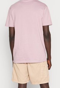 Camiseta de algodón de manga corta y cuello redondo en color rosa claro, combinada con pantalones cortos de carga beige con bolsillos laterales y un ajuste relajado.