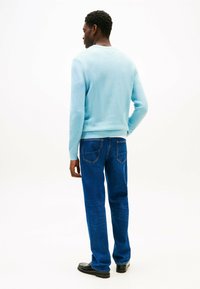 Maglione a maglia blu chiaro con polsini e orlo a costine, abbinato a jeans in denim blu scuro con tasche posteriori e taglio dritto.