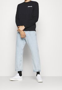 Svart långärmad sweatshirt med "Nike Air"-logga, tillsammans med ljusblå denimjeans och vita sneakers. Avslappnad passform med uppvikta ärmslut.