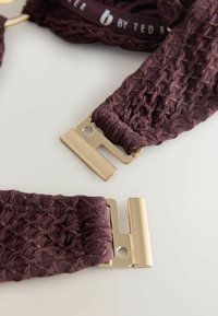 Fioletowa tkanina o fakturze z akcentami ze złotej nici, ozdobiona metalowymi zatrzaskami. Wzór zawiera pleciony motyw dla dodatkowego efektu.