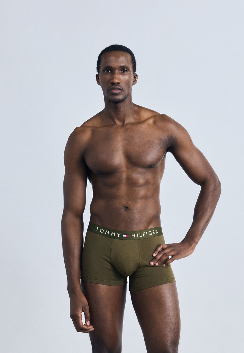 Πράσινα βαμβακερά ανδρικά μπόξερ με λευκή μέση που φέρει λογότυπο, εφαρμοστή σχεδίαση και λείο υφή, φορεμένα από άντρα μοντέλο σε ανοιχτό φόντο.