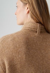 Pull en maille couleur chameau avec un col haut et un design texturé côtelé. Matière douce avec une coupe décontractée et des détails minimalistes.