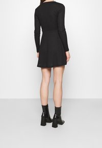 Svart ribbad långärmad klänning med figurnära bodice och utsvängd kjol. Har en rund halsringning och en strukturerad yta. Bärs med svarta klackskor.