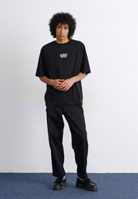 Sort oversized t-shirt med et lille logo, parret med sorte bukser og sorte sko. Enkel design med en afslappet pasform. Glat tekstur.