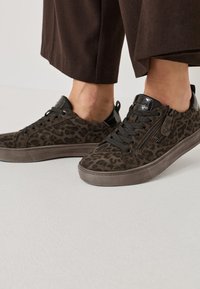 Brūni leopardu raksta sporta apavi ar teksturētu zamša materiālu, melniem akcentiem un auklām. Sānu rāvējslēdzēja detaļa, gumijas zole un noapaļots purns.
