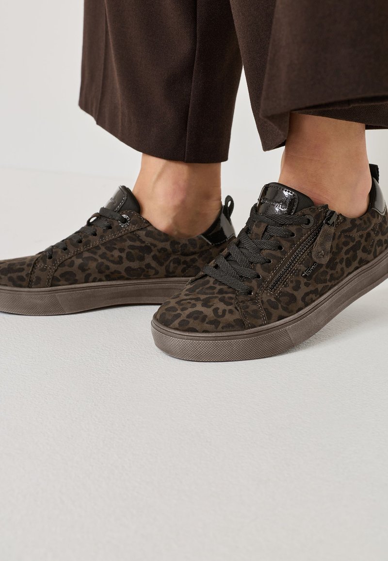 Brūni leopardu raksta sporta apavi ar teksturētu zamša materiālu, melniem akcentiem un auklām. Sānu rāvējslēdzēja detaļa, gumijas zole un noapaļots purns.
