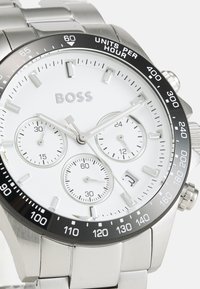 Reloj de acero inoxidable plateado con esfera blanca, bisel negro y tres subesferas. Cuenta con una ventana de fecha y marcadores de hora aplicados.
