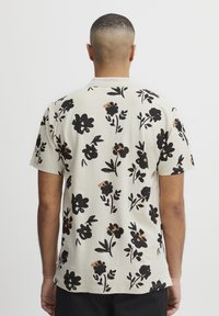 Kortermet t-skjorte i lys beige med svart blomsterdesign og brune detaljer. Laget av bomull, casual passform, rund halsdesign.