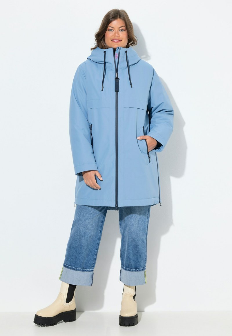 Ljusblå vattentät parkas med huva, framdragkedja, två sidofickor och svarta snoddar. Bärs över avkortade denimjeans och stövlar.
