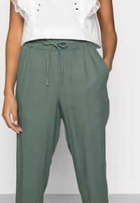Pantalones de mezcla de lino verdes con cintura elástica y cordón, bolsillos frontales y un ajuste relajado. Textura suave y material transpirable.